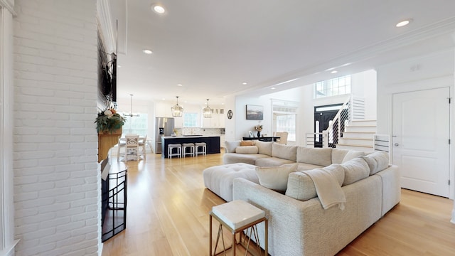 living room featuring a chandelier, crown molding, light hardwood / wood-style floors, and brick wall