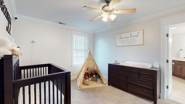 bedroom featuring ceiling fan, crown molding, light carpet, a nursery area, and connected bathroom