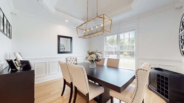 dining area with ornamental molding, light wood-type flooring, a tray ceiling, and an inviting chandelier