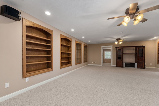 unfurnished living room with carpet flooring, built in shelves, and ceiling fan