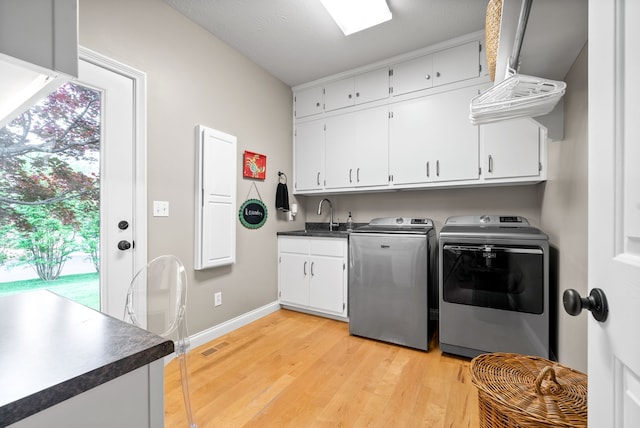 clothes washing area with cabinets, washing machine and dryer, a healthy amount of sunlight, and light wood-type flooring