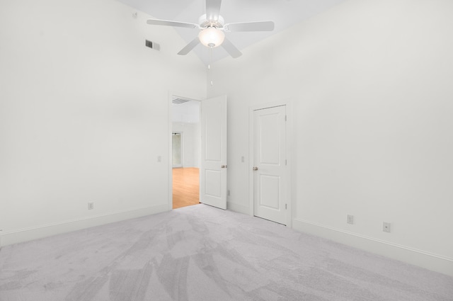 unfurnished room with light carpet, a towering ceiling, and ceiling fan