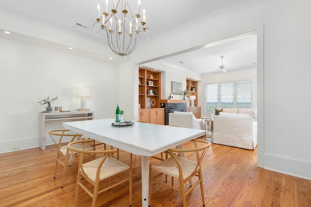 dining room featuring ceiling fan with notable chandelier, light hardwood / wood-style flooring, and a stone fireplace