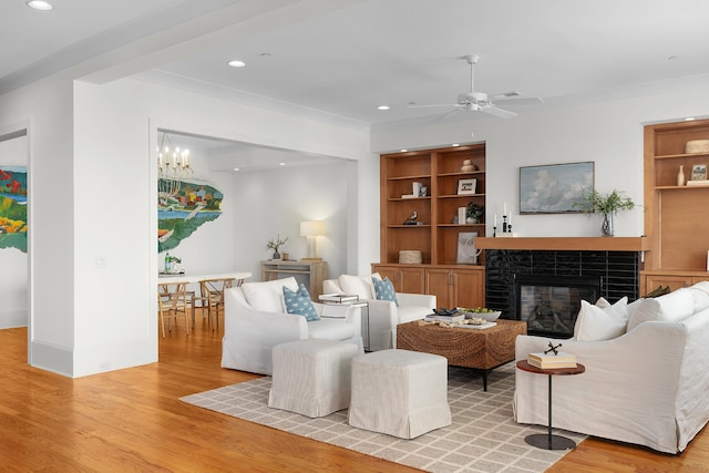 living room featuring a tiled fireplace, ceiling fan, and light hardwood / wood-style flooring