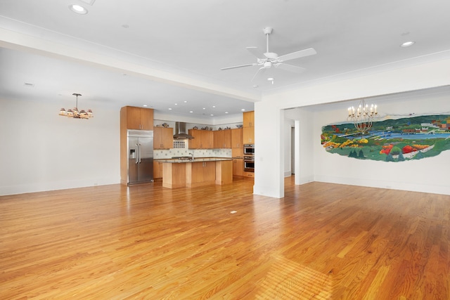 unfurnished living room with ceiling fan with notable chandelier and light wood-type flooring