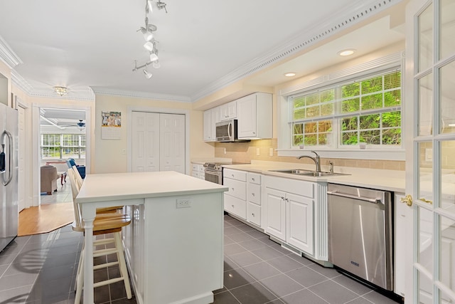 kitchen with dark tile patterned floors, white cabinets, stainless steel appliances, sink, and ornamental molding