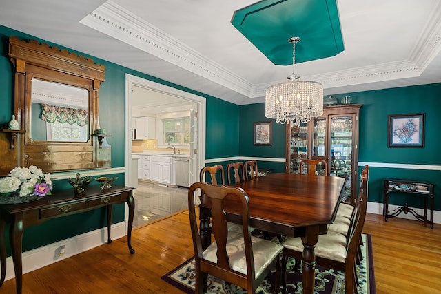 dining room with a notable chandelier, a tray ceiling, wood-type flooring, sink, and ornamental molding