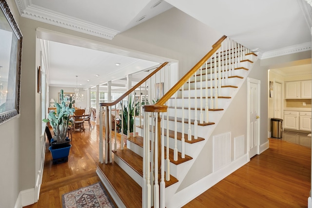 stairway featuring an inviting chandelier, wood-type flooring, and crown molding