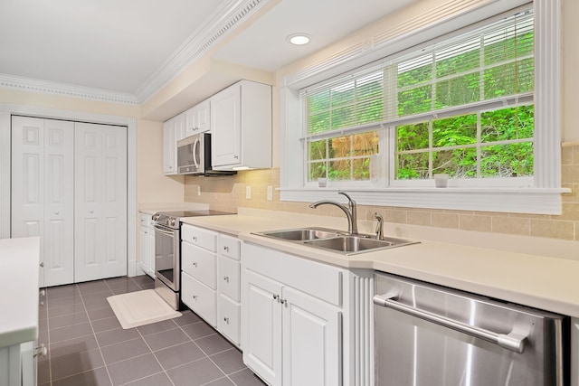 kitchen with crown molding, white cabinets, appliances with stainless steel finishes, dark tile patterned flooring, and sink