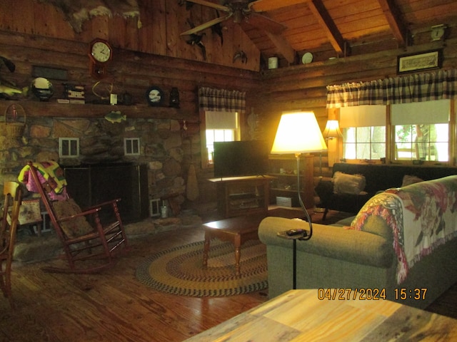 living room featuring beamed ceiling, ceiling fan, a fireplace, wood-type flooring, and rustic walls