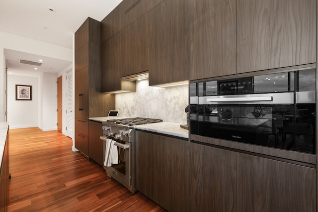 kitchen featuring exhaust hood, appliances with stainless steel finishes, tasteful backsplash, hardwood / wood-style floors, and dark brown cabinetry