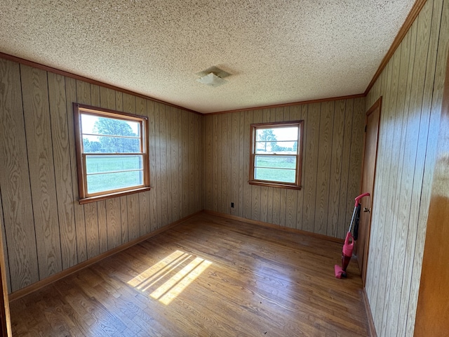 empty room with hardwood / wood-style flooring, crown molding, wooden walls, and a textured ceiling