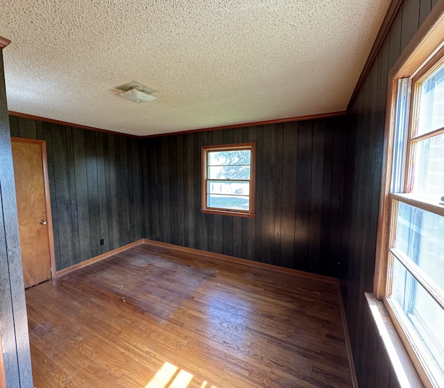 spare room featuring wood-type flooring, a textured ceiling, wood walls, and crown molding