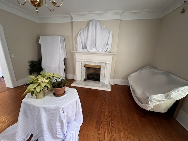 living room featuring dark hardwood / wood-style floors, a stone fireplace, crown molding, and a chandelier