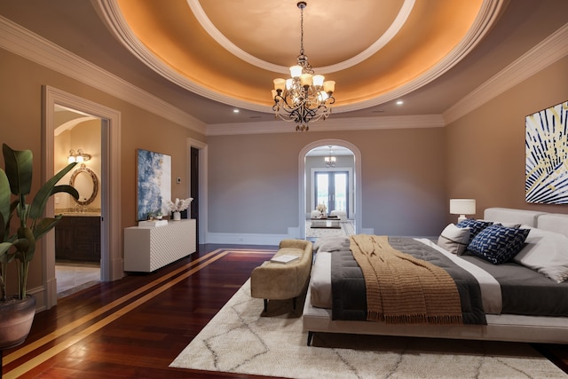 bedroom with ensuite bathroom, dark hardwood / wood-style flooring, a tray ceiling, ornamental molding, and a notable chandelier