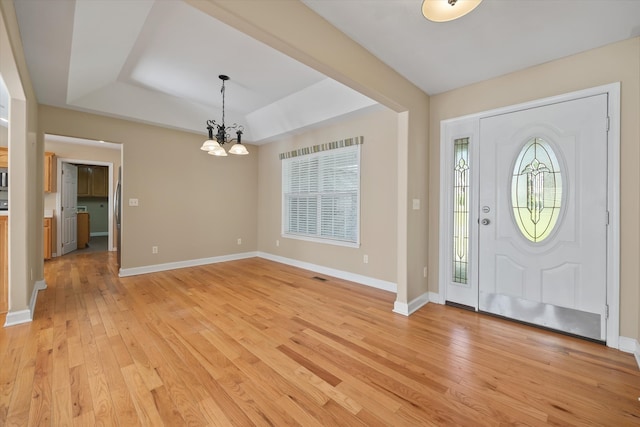 entrance foyer featuring light hardwood / wood-style floors, a tray ceiling, and an inviting chandelier