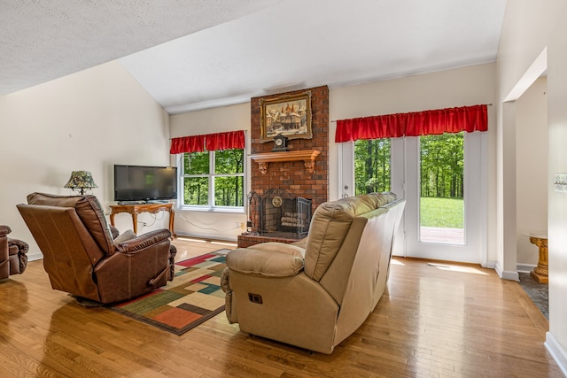 living room with a fireplace, a textured ceiling, light hardwood / wood-style flooring, and a healthy amount of sunlight