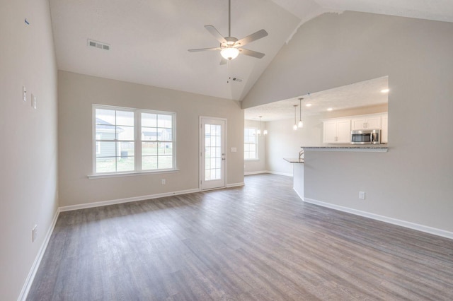 unfurnished living room featuring ceiling fan with notable chandelier, high vaulted ceiling, and dark hardwood / wood-style flooring