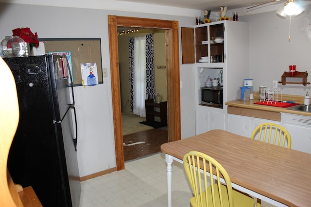 kitchen with ceiling fan, white cabinetry, black refrigerator, sink, and light tile floors