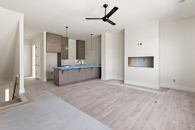 kitchen featuring a breakfast bar area, pendant lighting, ceiling fan, light hardwood / wood-style flooring, and sink