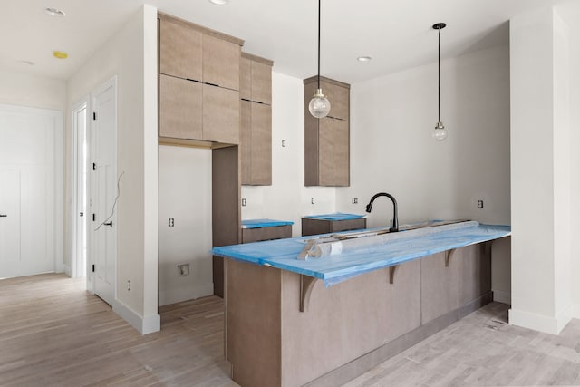 kitchen with kitchen peninsula, pendant lighting, light wood-type flooring, a kitchen bar, and sink