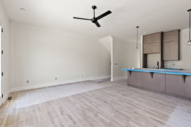 kitchen with ceiling fan, hanging light fixtures, sink, a kitchen breakfast bar, and light wood-type flooring