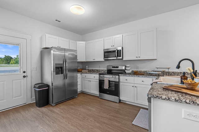 kitchen featuring appliances with stainless steel finishes, white cabinets, a sink, and wood finished floors