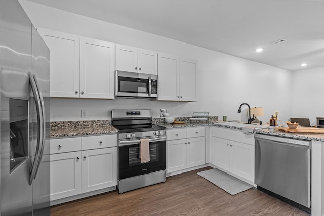 kitchen with dark wood finished floors, stainless steel appliances, visible vents, a sink, and dark stone counters