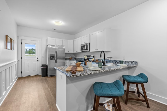 kitchen with a peninsula, appliances with stainless steel finishes, wood finished floors, and white cabinetry