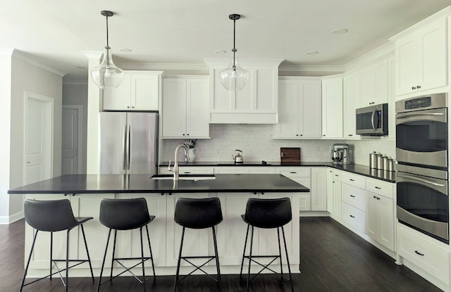 kitchen with sink, appliances with stainless steel finishes, an island with sink, pendant lighting, and white cabinets