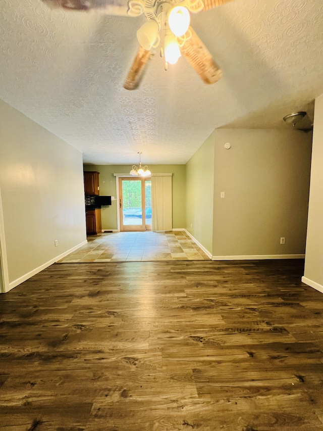 empty room with dark wood-type flooring, ceiling fan with notable chandelier, and a textured ceiling