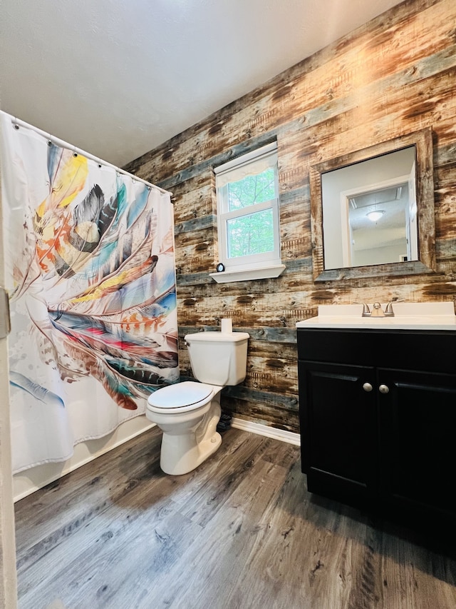 bathroom with toilet, hardwood / wood-style floors, wooden walls, and vanity