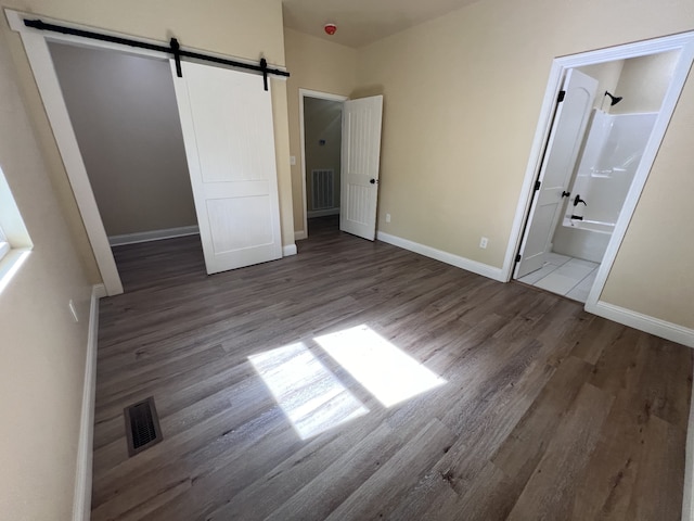 unfurnished bedroom with wood-type flooring, ensuite bath, a barn door, and a closet