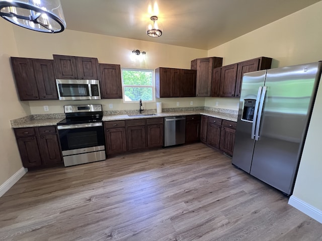 kitchen with dark brown cabinetry, appliances with stainless steel finishes, sink, light hardwood / wood-style floors, and a notable chandelier