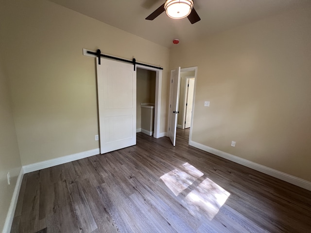 unfurnished bedroom with a barn door, ceiling fan, and dark hardwood / wood-style floors