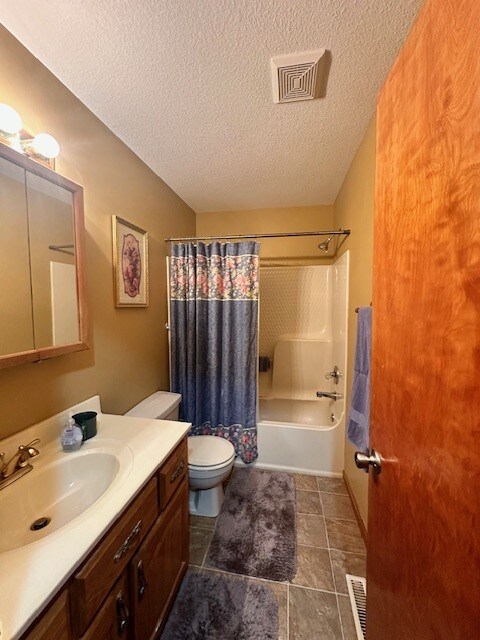 full bathroom with vanity, toilet, shower / bath combo with shower curtain, and a textured ceiling