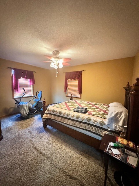 carpeted bedroom with ceiling fan and a textured ceiling