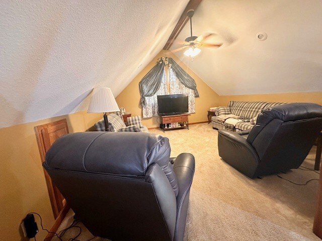 carpeted home theater room with ceiling fan, a textured ceiling, and vaulted ceiling with beams