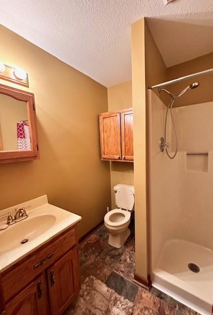 bathroom with vanity, toilet, a textured ceiling, and walk in shower