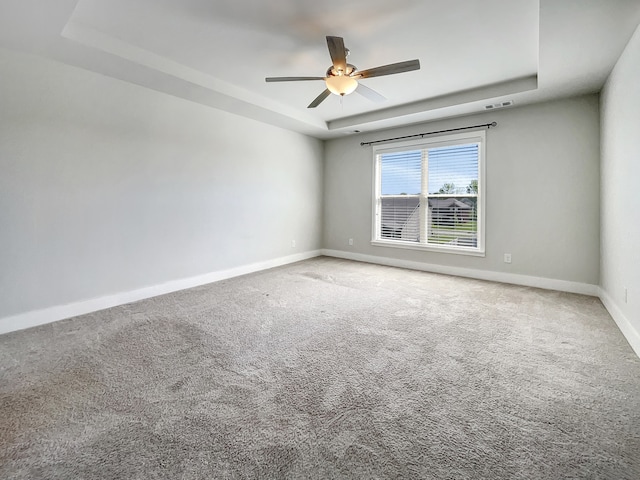 carpeted empty room featuring ceiling fan and a raised ceiling