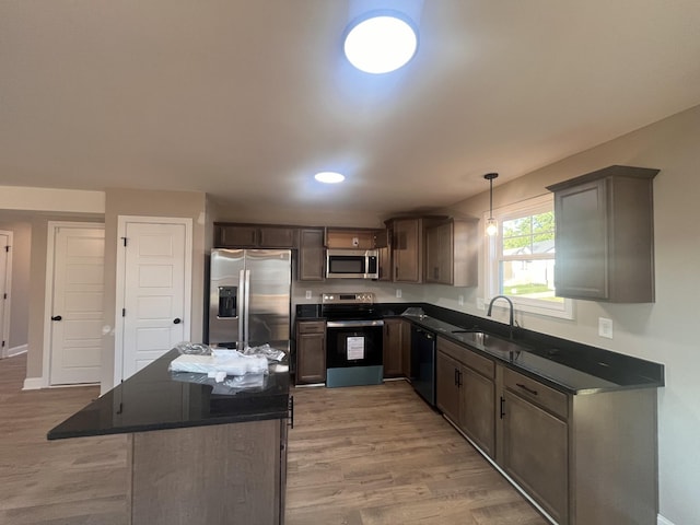 kitchen with hanging light fixtures, sink, stainless steel appliances, and light hardwood / wood-style floors