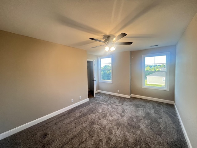 unfurnished room featuring dark colored carpet, a wealth of natural light, and ceiling fan