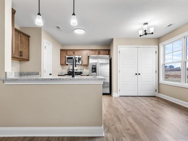 kitchen featuring light hardwood / wood-style flooring, hanging light fixtures, stainless steel appliances, light stone counters, and kitchen peninsula