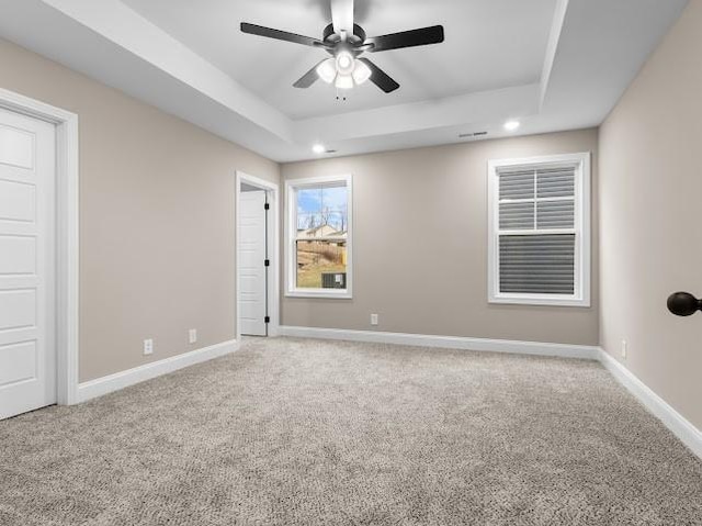 carpeted empty room with ceiling fan and a raised ceiling