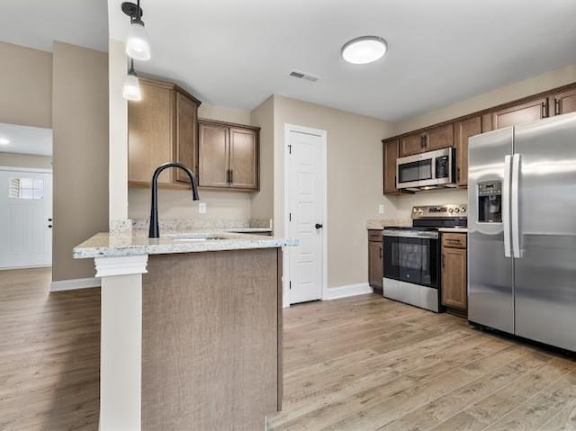 kitchen with light stone counters, stainless steel appliances, decorative light fixtures, and light wood-type flooring