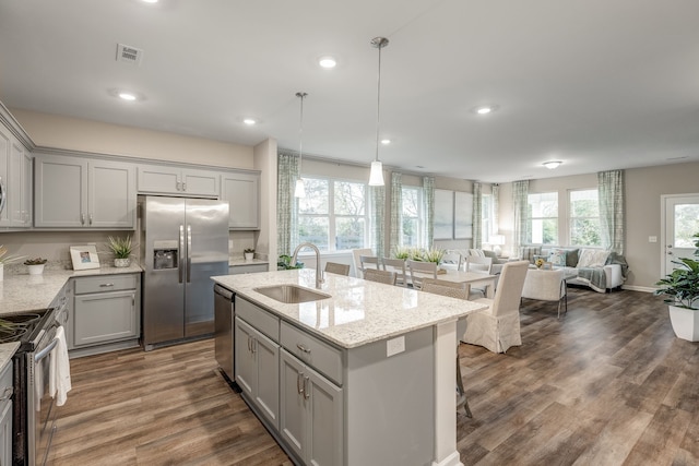 kitchen with appliances with stainless steel finishes, sink, hanging light fixtures, wood-type flooring, and a center island with sink