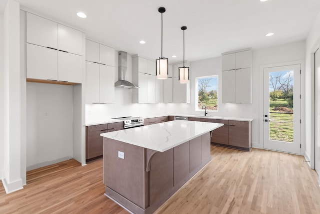 kitchen featuring wall chimney range hood, sink, hanging light fixtures, light wood-type flooring, and a kitchen island