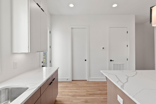 kitchen with light wood-type flooring, light stone countertops, and sink