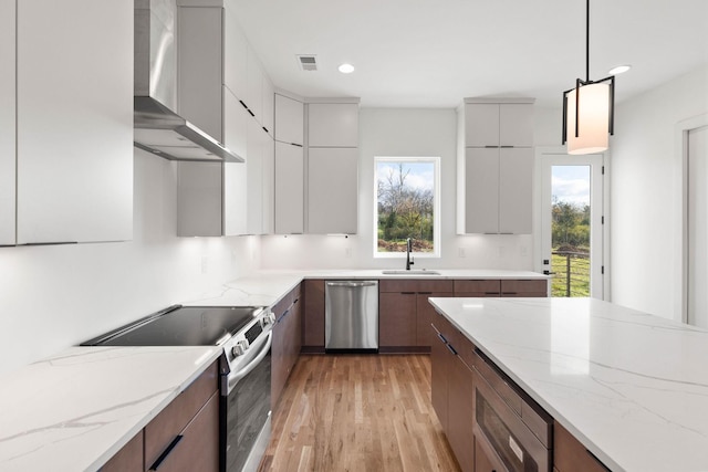 kitchen with pendant lighting, stainless steel appliances, light stone counters, and wall chimney range hood