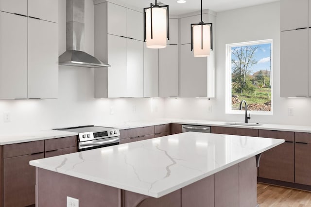 kitchen with pendant lighting, wall chimney range hood, sink, light stone countertops, and appliances with stainless steel finishes